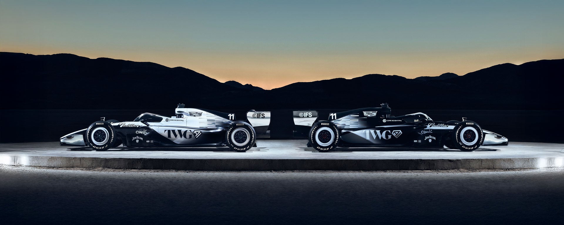 Two Cadillac Racing Cars Facing Outwards on a Circular Structure Outside in the Evening.
