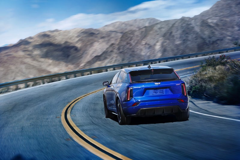 Rear View of a Blue 2026 OPTIQ-V Driving on a Curve of a Mountain Row | Star Cadillac in Quakertown PA