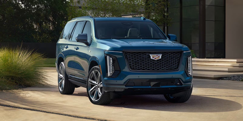 Blue Cadillac SUV parked on a driveway outside a modern building