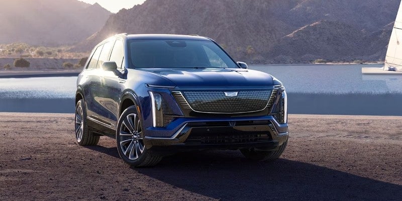 Blue Cadillac SUV parked beside a lake with mountains in the background
