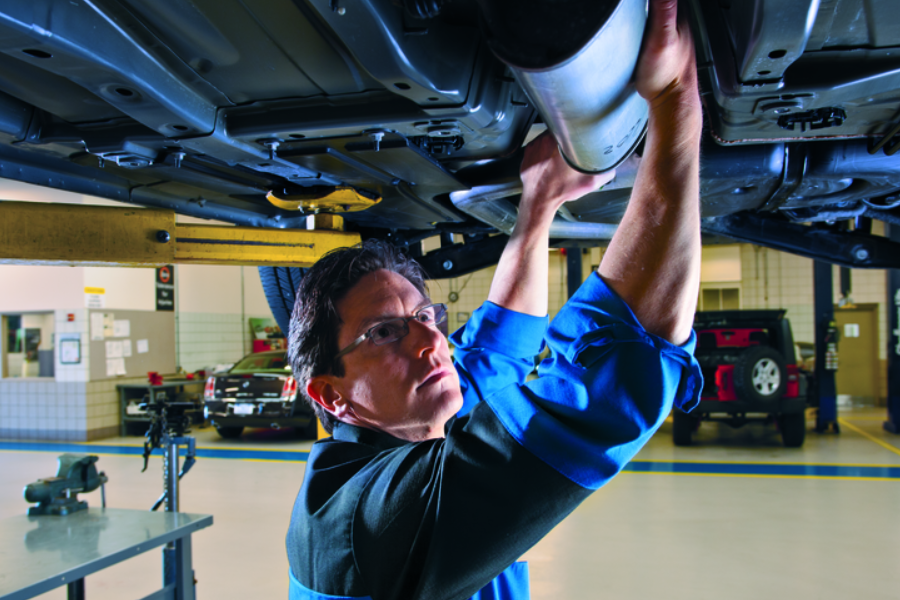 Automotive technician inspecting the underside of a vehicle in a service bay