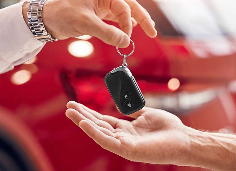 Car key fob being handed from one person to another in front of a red vehicle